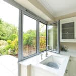 Thumbnail of http://A%20modern%20kitchen%20with%20white%20cabinets%20and%20a%20marble%20countertop,%20featuring%20an%20open%20window%20overlooking%20a%20patio%20and%20a%20lush%20garden.