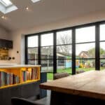 Thumbnail of http://Modern%20kitchen%20with%20skylights,%20a%20wooden%20table,%20shelves%20with%20books,%20and%20floor-to-ceiling%20windows%20overlooking%20a%20backyard%20with%20a%20playhouse%20and%20trees.