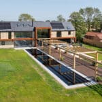 Thumbnail of http://Modern%20two-story%20house%20with%20solar%20panels,%20large%20windows,%20and%20wooden%20accents.%20Features%20a%20long%20reflecting%20pool,%20pergola,%20and%20surrounding%20lawn%20with%20trees%20under%20a%20clear%20blue%20sky.