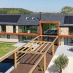 Thumbnail of http://Modern%20two-story%20house%20with%20solar%20panels,%20stone%20and%20glass%20exterior,%20surrounded%20by%20green%20lawn.%20Features%20a%20wooden%20pergola%20and%20patio%20area%20with%20outdoor%20furniture.