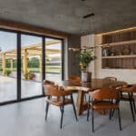Thumbnail of http://Modern%20dining%20room%20with%20a%20wooden%20table,%20six%20brown%20chairs,%20and%20a%20potted%20plant.%20Large%20glass%20doors%20open%20to%20a%20patio%20with%20outdoor%20seating%20and%20a%20view%20of%20greenery.%20Wood%20shelving%20with%20decor%20on%20the%20wall.