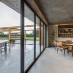 Thumbnail of http://Modern%20dining%20area%20with%20wooden%20accents%20next%20to%20large%20glass%20doors%20opening%20to%20a%20patio%20with%20chairs%20and%20pergola.%20Greenery%20is%20visible%20outside.