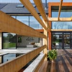 Thumbnail of http://Modern%20house%20with%20large%20glass%20windows%20and%20wooden%20beams%20overhead.%20A%20patio%20with%20wooden%20flooring%20and%20a%20potted%20plant%20leads%20to%20the%20entrance.