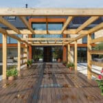 Thumbnail of http://Wooden%20pergola%20over%20a%20wet%20deck%20leading%20to%20a%20modern%20two-story%20brick%20house%20with%20large%20windows.%20Potted%20plants%20line%20the%20walkway.