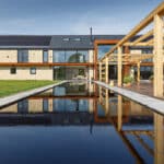 Thumbnail of http://Modern%20house%20with%20solar%20panels%20and%20large%20windows,%20featuring%20a%20reflective%20rectangular%20pool%20and%20a%20wooden%20pergola%20in%20the%20foreground,%20set%20in%20a%20grassy%20yard%20under%20a%20clear%20blue%20sky.