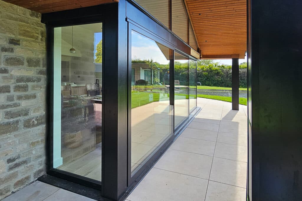 Corner of a modern house with large glass windows, stone wall, and a view of the green lawn outside.