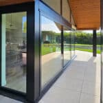 Thumbnail of http://Corner%20of%20a%20modern%20house%20with%20large%20glass%20windows,%20stone%20wall,%20and%20a%20view%20of%20the%20green%20lawn%20outside.