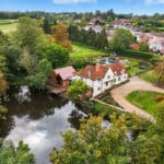 Thumbnail of http://Aerial%20view%20of%20Bouchiers%20Hall,%20a%20Grade%20II%20listed%2015th%20century%20historic%20home%20with%20white%20rendered%20walls,%20red%20tile%20roof,%20and%20modern%20extensions%20overlooking%20a%20river%20and%20countryside.