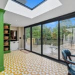 Thumbnail of http://Contemporary%20extension%20with%20Sunflex%20bifold%20doors%20opening%20onto%20wooden%20deck,%20featuring%20skylight,%20green%20cabinetry,%20and%20patterned%20flooring.
