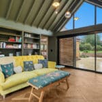 Thumbnail of http://Contemporary%20living%20room%20with%20yellow%20sofa%20and%20large%20sliding%20glass%20doors%20opening%20to%20courtyard%20garden%20and%20countryside%20views%20beyond.