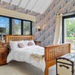 Thumbnail of http://Contemporary%20bedroom%20with%20bifold%20doors%20opening%20to%20garden,%20featuring%20patterned%20wallpaper,%20wooden%20bed%20frame,%20and%20modern%20glazing%20systems%20in%20historic%20setting.