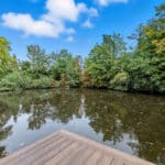 Thumbnail of http://Wooden%20deck%20overlooking%20tranquil%20river%20with%20dense%20woodland%20and%20mature%20trees%20reflected%20in%20still%20water%20under%20blue%20sky.