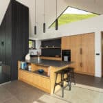 Thumbnail of http://Modern%20Cornish%20kitchen%20featuring%20wooden%20cabinetry,%20dark%20island%20with%20seating,%20and%20skylight%20openings%20providing%20natural%20light%20and%20views%20in%20the%20Myrio%20home.