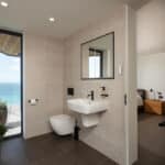 Thumbnail of http://Myrio%20Sennen%20Cove%20bathroom%20with%20coastal%20views%20through%20bifold%20doors,%20featuring%20white%20sanitaryware%20and%20neutral%20tiling.